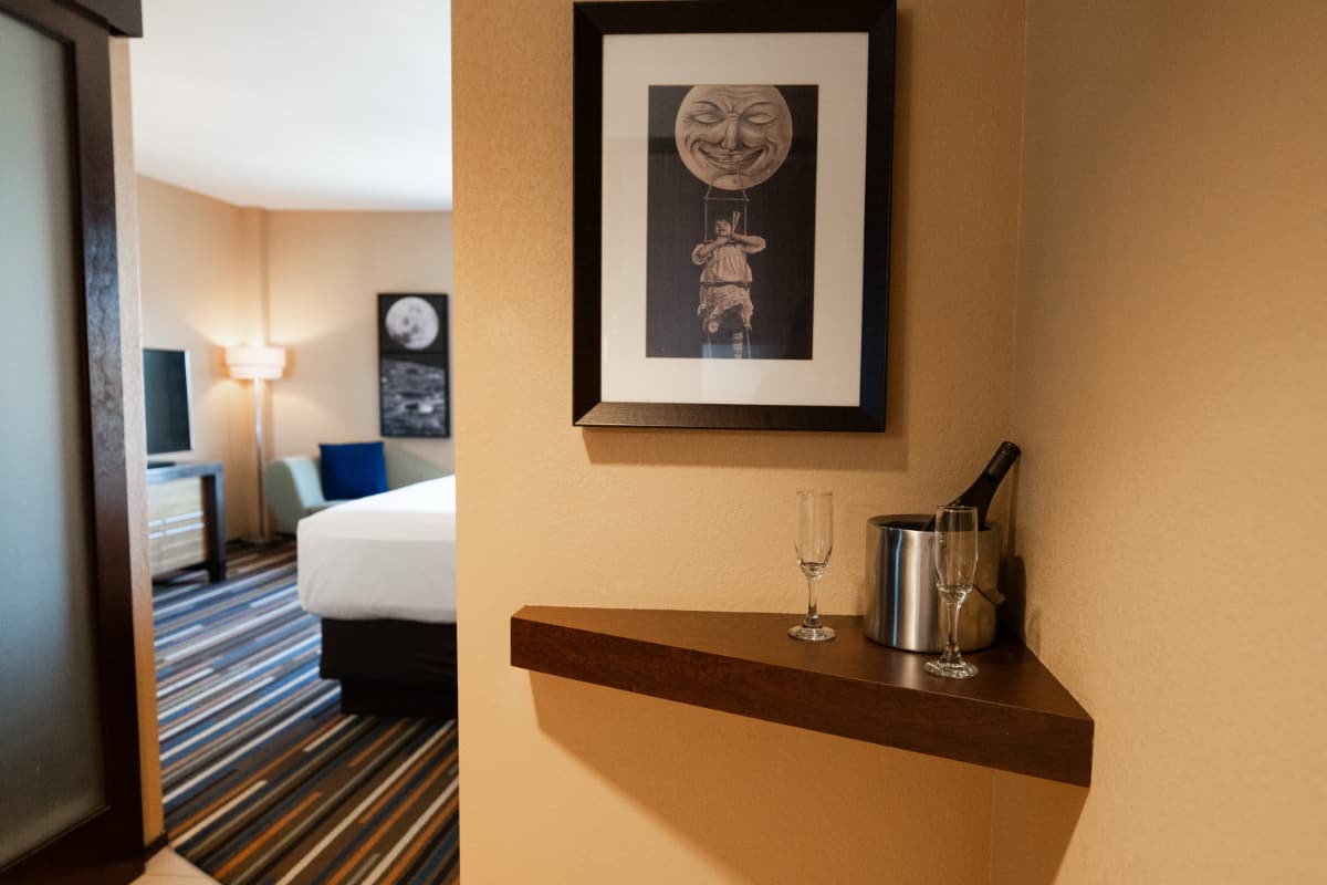 A bottle of champagne chills in an ice container, and two empty champagne flutes sit next to it. The rest of the hotel room is in the background.