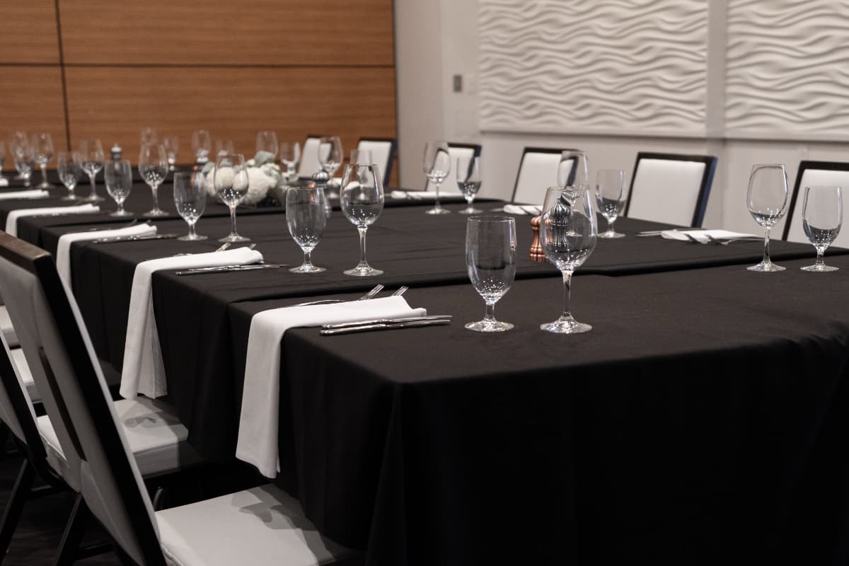 fancy table settings Tables with black table clothes and white napkins. The table has fancy glassware and is surrounded by white and black chairs.
