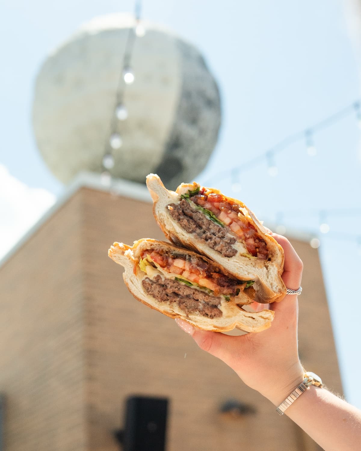 burger in front of moon Someone holds two halves of burger in front of the rooftop moon statue